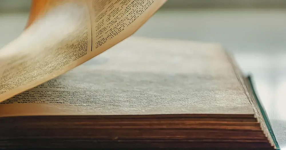 Livro aberto com páginas virando sobre a mesa